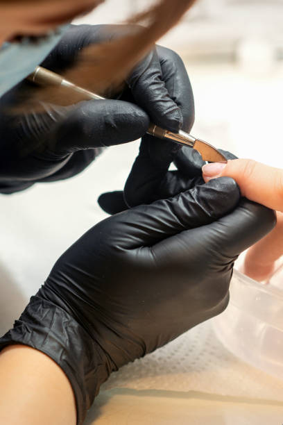 istock Close up professional manicurist master holding customer hand while using a cuticle pusher in a nail salon. 1440940455