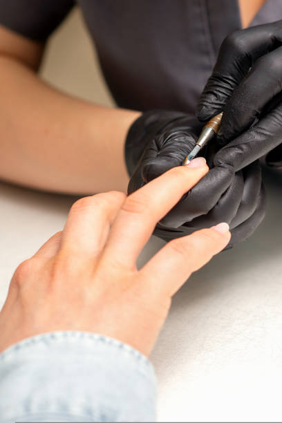 istock Close up professional manicurist master holding customer hand while using a cuticle pusher in a nail salon. 1440941415