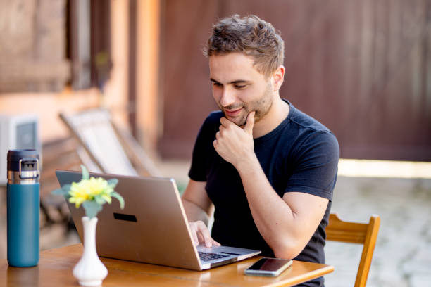 istock Smiling young man working on a laptop outside at a patio table 1440943425