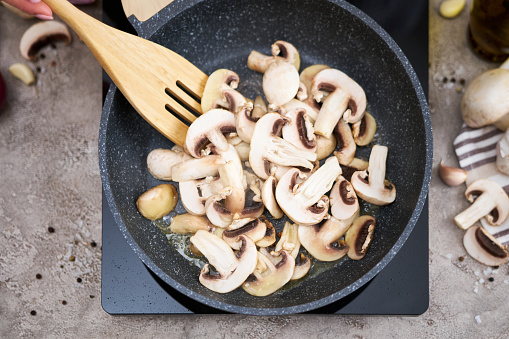 Sliced mushrooms in a frying pan on induction hob at domestic kitchen.