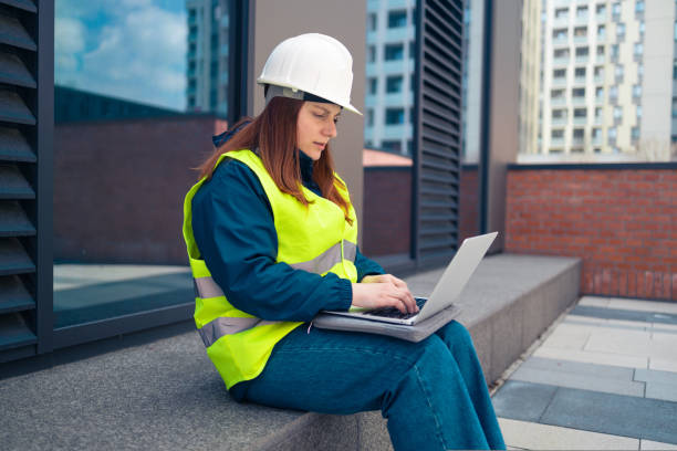 istock Female industrial engineers in hard hats discuss new project while using laptop at work on major construction site 1440945624