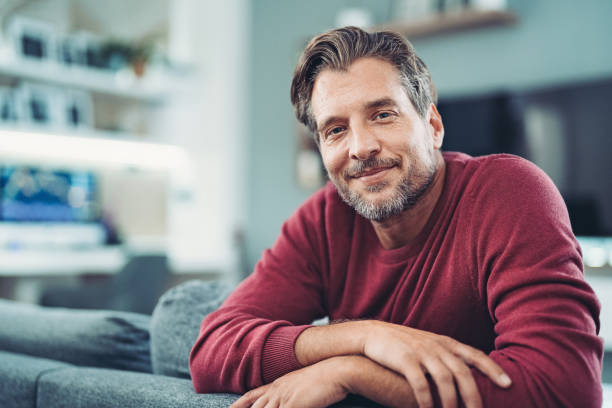 hombre sonriente de mediana edad disfrutando de un momento de relax en casa - barba de tres días fotografías e imágenes de stock