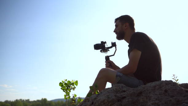 istock A young man sits on a stone with a camera in his hands. Man shoots at camera nature. 1440949149