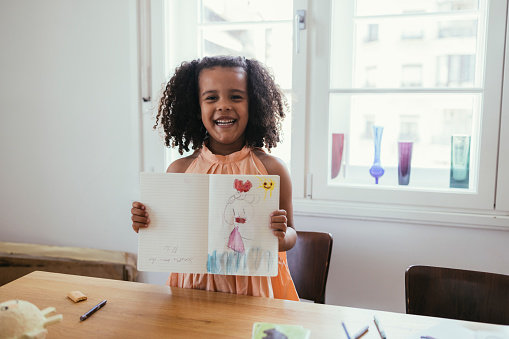 Portrait of a cute little Cuban girl showing her drawing to the camera.