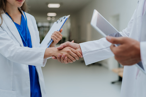 Close-up of doctors shaking hands at a hospital corridor.