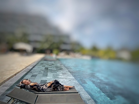 A beautiful young lady lying down beside the pool