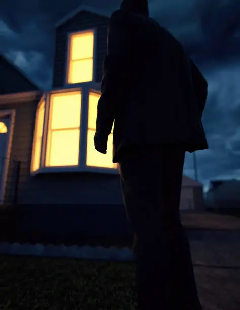 Photo of Lone man in suit by an illuminated house at dusk. Rear view. 3D render.