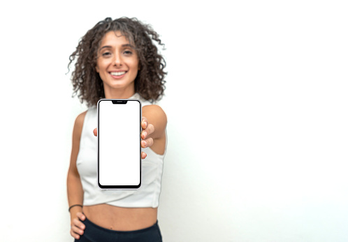 Beautiful curly hair woman in front of wall holding smartphone with blank screen