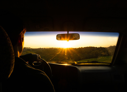 A closeup shot of a Hispanic young male driving a car with the sun rising in the horizon
