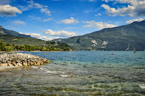 river Sarca flows into lake garda, Riva, Nago, Torbole. landscape with water, mountains, blue sky, clouds, beach, shore