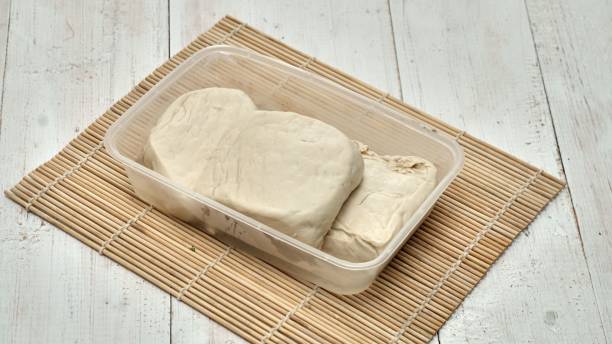High-angle shot of raw tofu pieces on a plastic container on a wooden mat