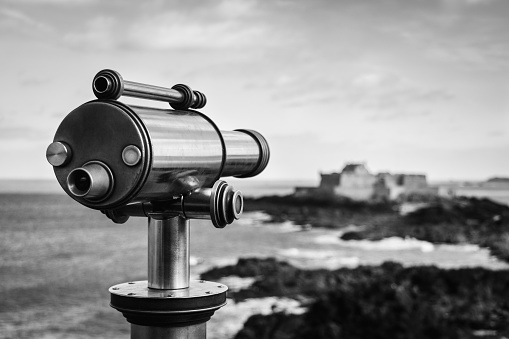A beautiful greyscale view of a telescope set in front of the beach