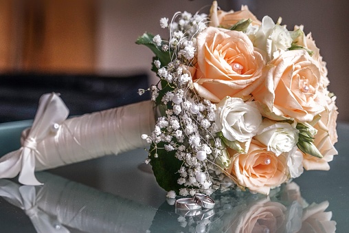 a Closeup of a wedding bouquet next to wedding rings on glass