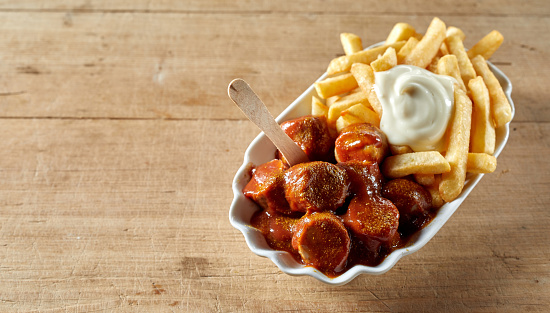 A from above of tasty curried sausage chunks with hot chips and mayonnaise in bowl with eco stick on brown background