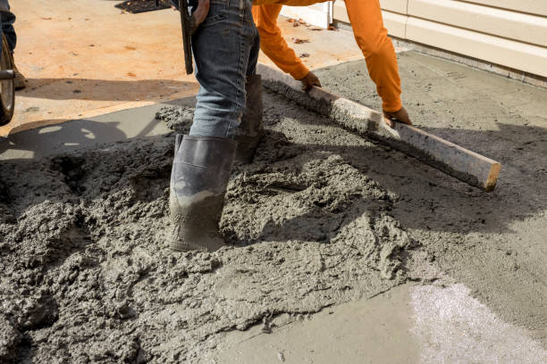 The workers construct a new sidewalk adjacent to the house by pouring cement on the side of the house as part of the construction process stock photo