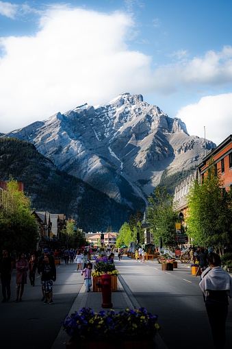 Banff, Canada – July 07, 2022: A vertical shot of people walking on Banff Avenue with the background of Cascade mountain in Banff Canada