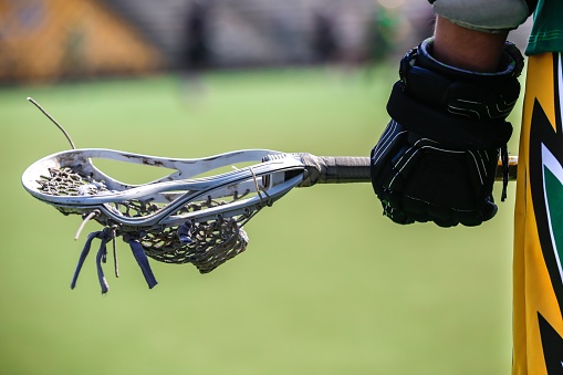 Looking down on a pair of Lacrosse sticks and a white ball sitting on the white Midfield-line of an artificial turf sports field.