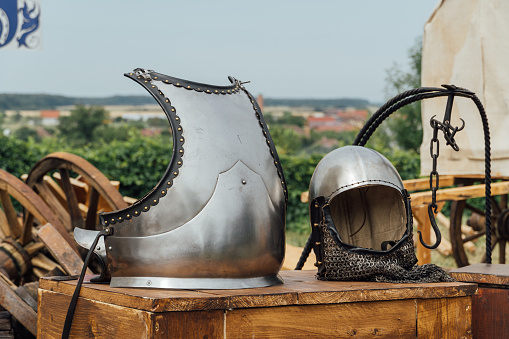 A closeup shot of an old medieval knight metal helmet and breastplate put outside on a wood