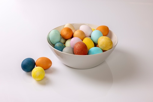 A closeup of colourfully painted Easter eggs in a ceramic bowl on with two my