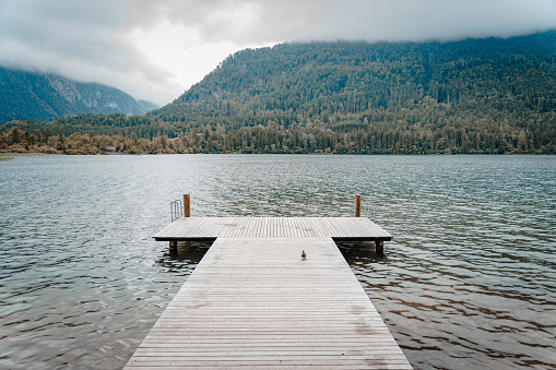 A dock on a lake or a river surrounded by forests on hills on a cloudy day