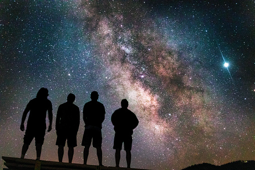 A silhouette shot of four friends watching the beautiful milky way in the night sky