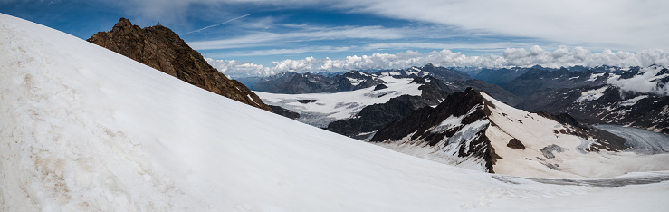 A beautiful panoramic shot of Weisskugel with snow covering its peak under a bright sky in Italy/Austria