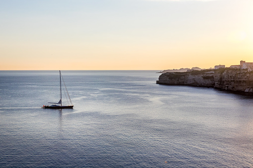 A lone boat sailing towards the shore on a calm sea in Corsica, France under a clear sky at sunset