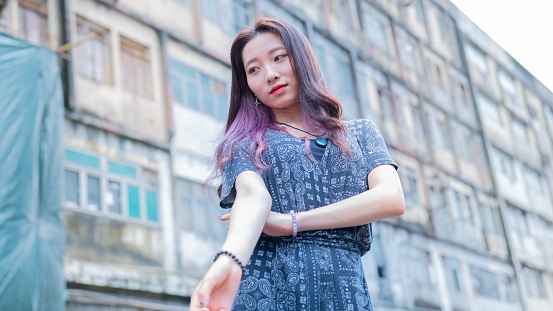 A low angle shot of an Asian female with purple hair posing outdoors