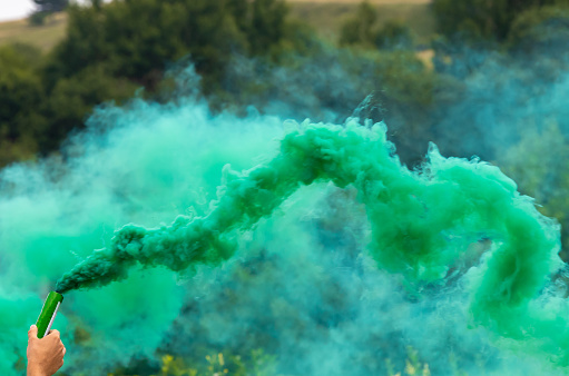 A person holding a green-colored smoke bomb in the air