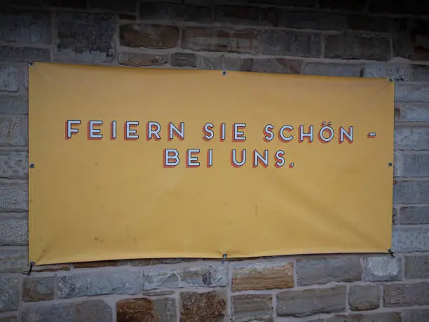 A yellow banner with "feiern sie schon bei uns" (have fun with us) text on a brick wall