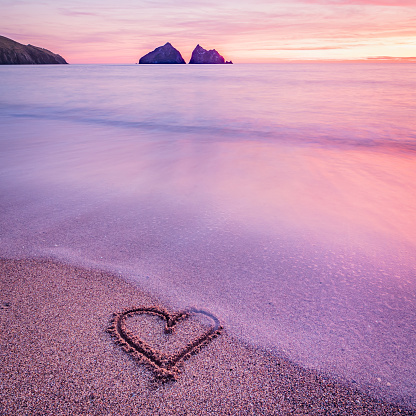 A heart carved into sand on a seashore at sunset