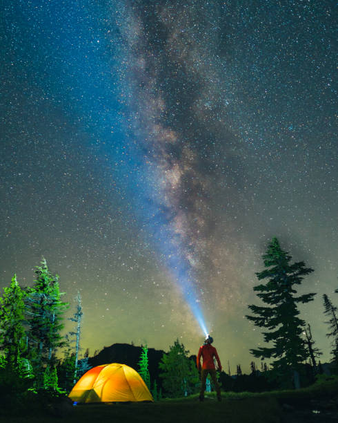 istock Vertical shot of a hiker with a headlight watching the galaxy sky over a camping site with a tent 1440974923