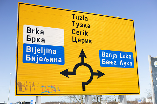 Brcko district, Bosnia and Herzegovina – August 21, 2019: A yellow road sign in Brcko district in Latin and Cyrillic alphabets showing the destinations of several settlements