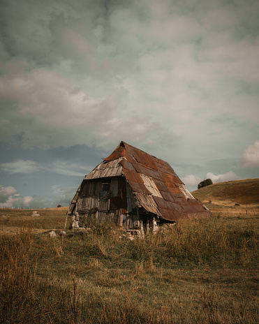 A scenic view of an old barn in the middle of a field in the countryside under a gloomy sky