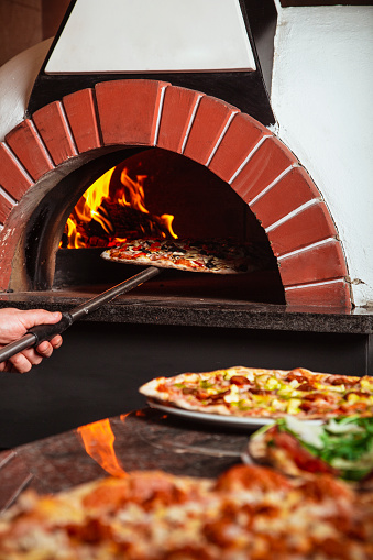 A vertical shot of traditional Italian pizza cooking in a wood stone oven