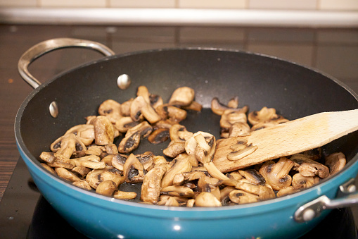 A tasty champignon mushrooms being cooked in a blue pan