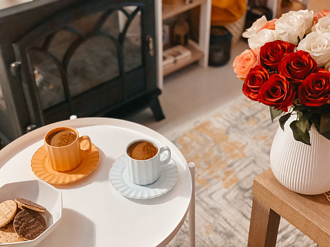 A beautiful shot of two cups of coffee and a bouquet of colorful fresh roses