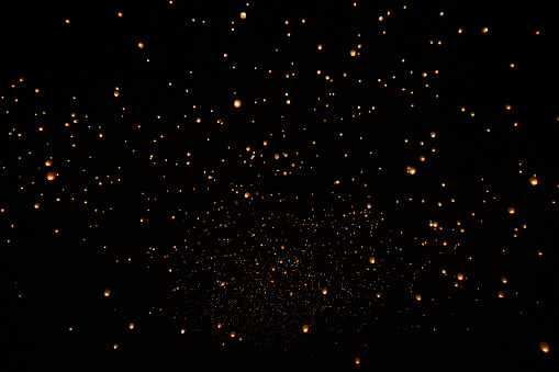 A dark sky with many floating orange lanterns