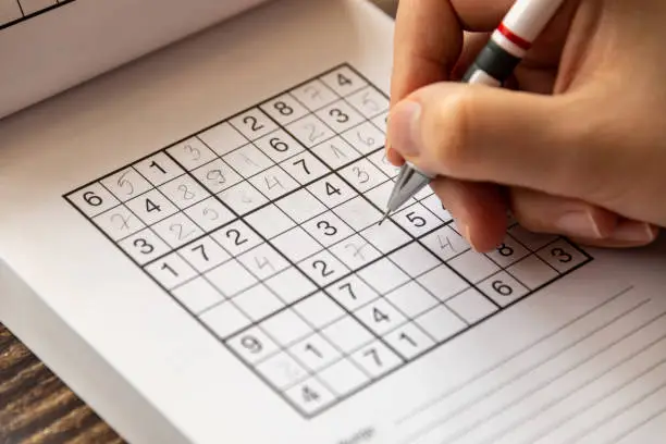 A person solving a sudoku puzzle on a wooden table