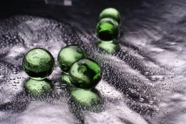A closeup of a green orbeez on a wet silver surface