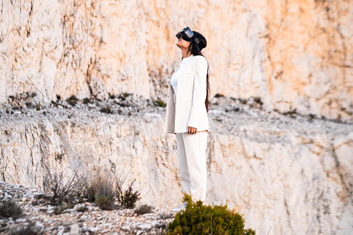 An elegant woman dressed in a white suit using a virtual reality goggles