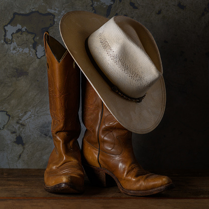 A closeup of a pair of old cowboy boots and a dusty Stetson