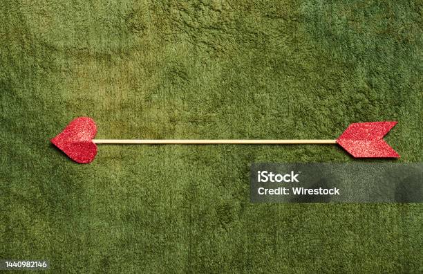 Closeup Shot Of A Cupid Arrow On A Green Lawn Stock Photo - Download Image Now - Cupid, Green Color, Arrow - Bow and Arrow