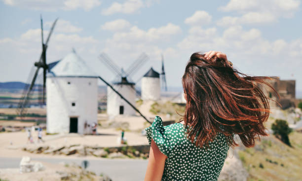 vista posteriore di una giovane donna in posa contro famosi vecchi mulini a vento nella città di consuegra, spagna - la mancha foto e immagini stock