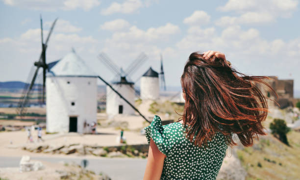 вид сзади молодой женщины, позирующей на фоне знаменитых старых ветряных мельниц в городе консуэгра, испания - la mancha стоковые фото и изображения