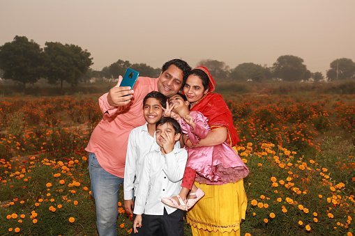 Larger Indian family standing together in flower field and taking selfie using smartphone during springtime.