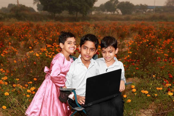 Three elementary child of Indian ethnicity using laptop together outdoor in flower field during springtime