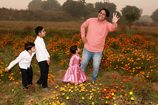 Cheerful farmer family portrait with hand raised outdoor in flower field.