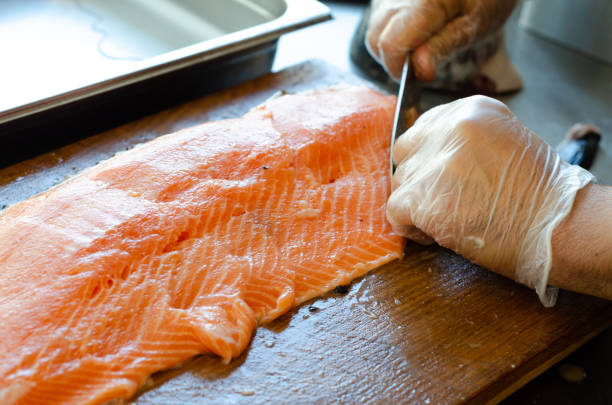 istock Chef cutting a salmon with a knife on a wooden board 1440985652