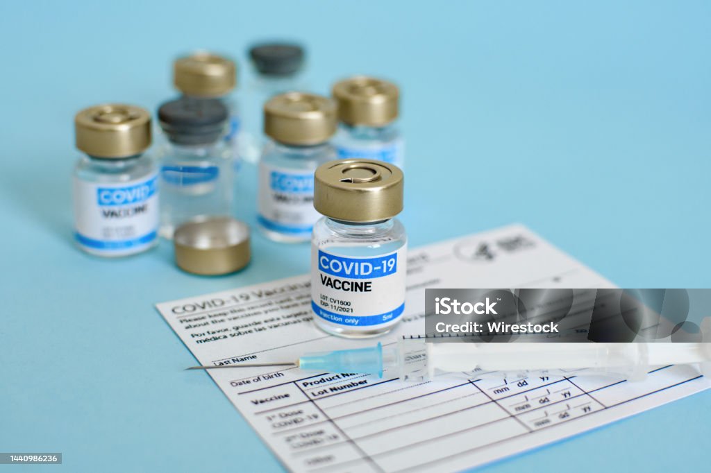 Close-up image of vaccine vial and syringe on CDC covid-19 vaccination record card. Covid-19 vaccine vial and syringe on CDC vaccination record card on blue background. COVID-19 Stock Photo